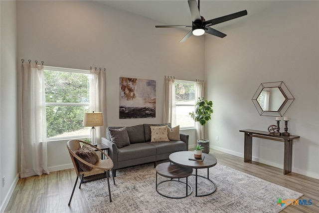 living room featuring a towering ceiling, ceiling fan, a healthy amount of sunlight, and light hardwood / wood-style flooring