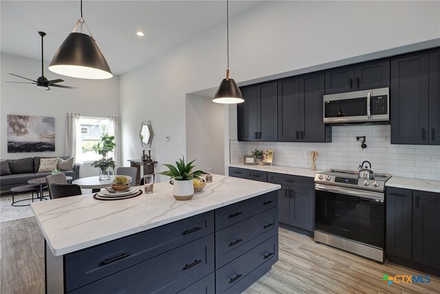 kitchen featuring a center island, stainless steel appliances, pendant lighting, decorative backsplash, and light hardwood / wood-style flooring