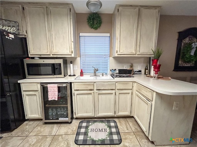 kitchen featuring sink, black refrigerator, kitchen peninsula, cream cabinetry, and beverage cooler