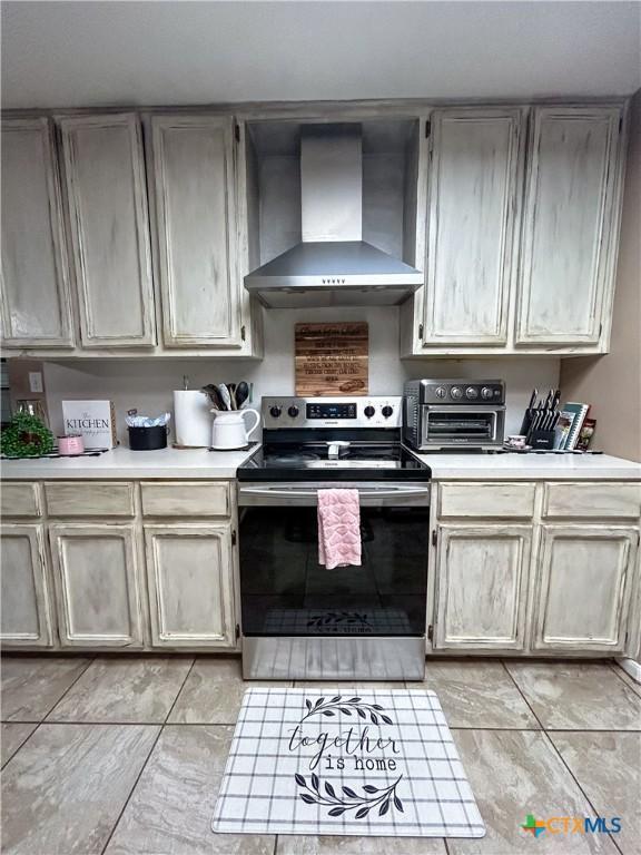 kitchen with light tile patterned floors, stainless steel electric stove, and wall chimney exhaust hood