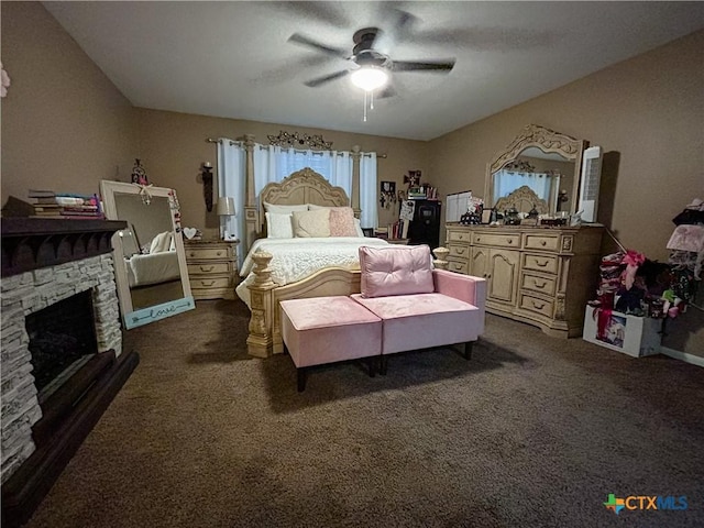 bedroom featuring a stone fireplace, dark carpet, and ceiling fan