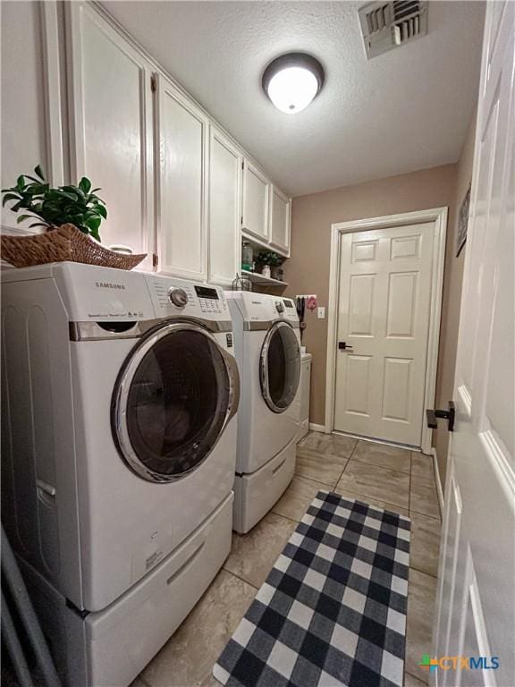 laundry area with cabinets, washer and clothes dryer, a textured ceiling, and light tile patterned floors