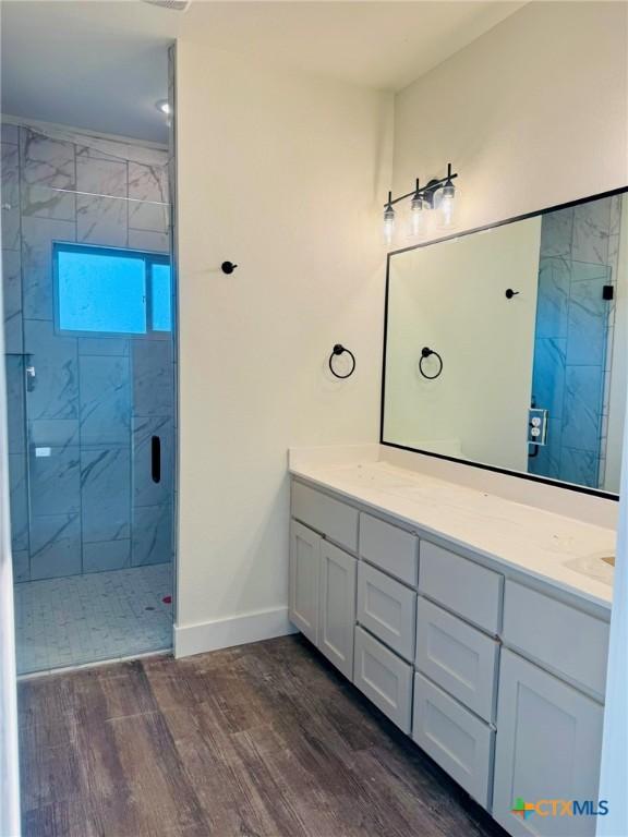 bathroom featuring hardwood / wood-style flooring, tiled shower, and vanity