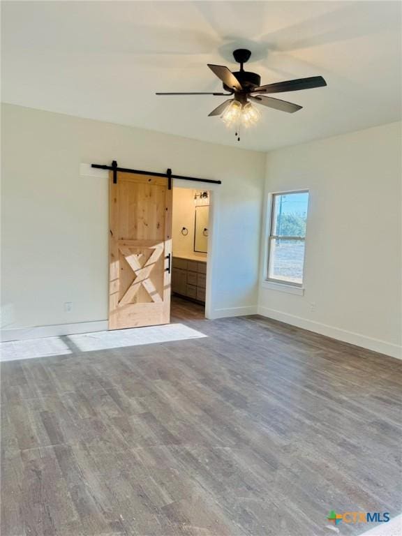 interior space featuring ceiling fan, ensuite bathroom, a barn door, and wood-type flooring