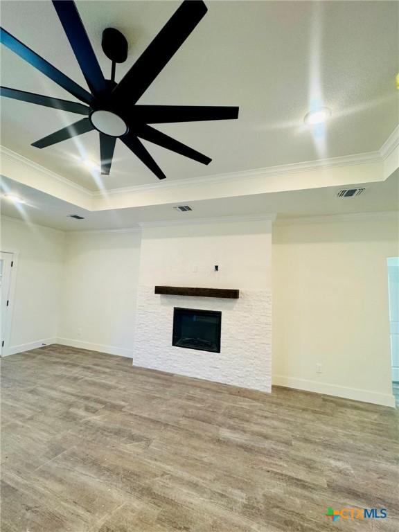 unfurnished living room featuring hardwood / wood-style flooring, ornamental molding, a raised ceiling, and ceiling fan