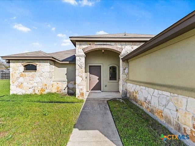 entrance to property with stone siding, roof with shingles, stucco siding, and a yard