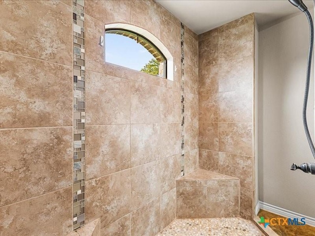 bathroom with baseboards and tiled shower