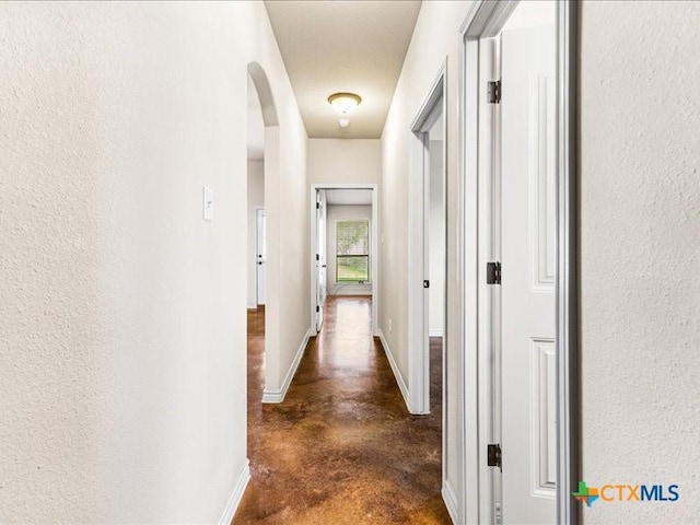 hall featuring arched walkways, baseboards, and finished concrete floors