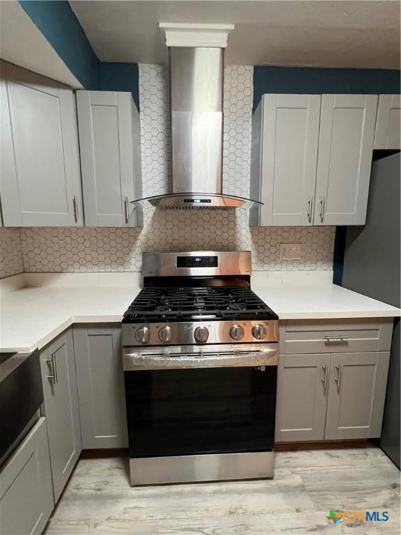 kitchen featuring decorative backsplash, wall chimney exhaust hood, stainless steel range with gas cooktop, and gray cabinetry