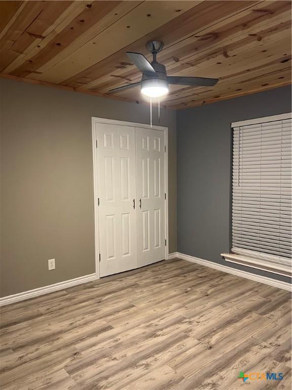 unfurnished bedroom featuring ceiling fan, light wood-type flooring, wood ceiling, and a closet