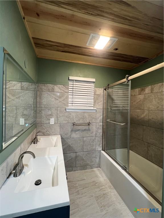 bathroom featuring combined bath / shower with glass door, wooden ceiling, tile patterned flooring, tile walls, and vanity