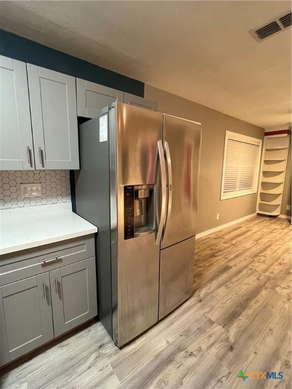 kitchen with tasteful backsplash, light wood-type flooring, stainless steel fridge, and gray cabinetry