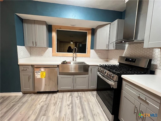 kitchen with dishwashing machine, wall chimney exhaust hood, sink, stainless steel range with gas cooktop, and gray cabinetry