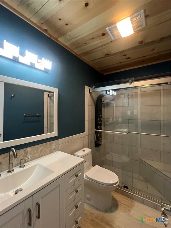 bathroom with toilet, wood ceiling, a shower with door, tile walls, and vanity