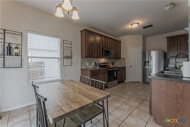 kitchen with sink, appliances with stainless steel finishes, light tile patterned floors, an inviting chandelier, and backsplash