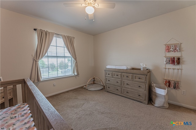 bedroom with ceiling fan, a crib, and light colored carpet