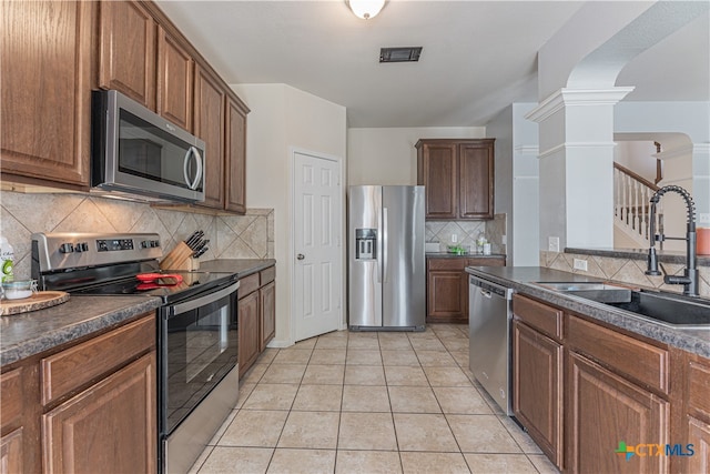 kitchen featuring stainless steel appliances, sink, light tile patterned floors, decorative columns, and decorative backsplash