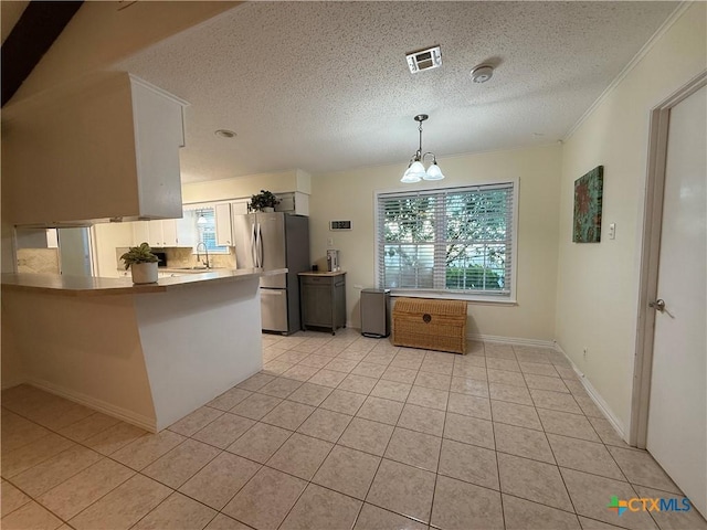 1001 Brookhollow Dr, Port Lavaca, TX 77979 - kitchen featuring freestanding refrigerator, a peninsula, a textured ceiling, light tile patterned floors, and white cabinetry