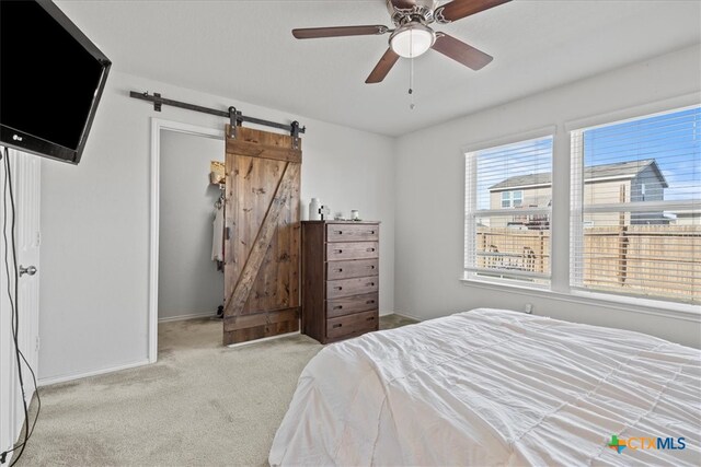 carpeted bedroom with a barn door and ceiling fan