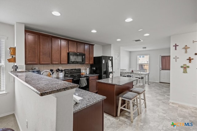 kitchen featuring black appliances, dark stone counters, a kitchen island, a breakfast bar area, and kitchen peninsula