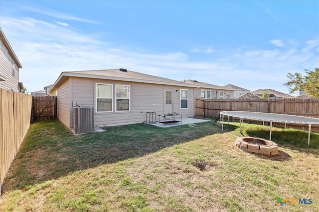 rear view of property featuring an outdoor fire pit, central AC, a patio area, a trampoline, and a yard