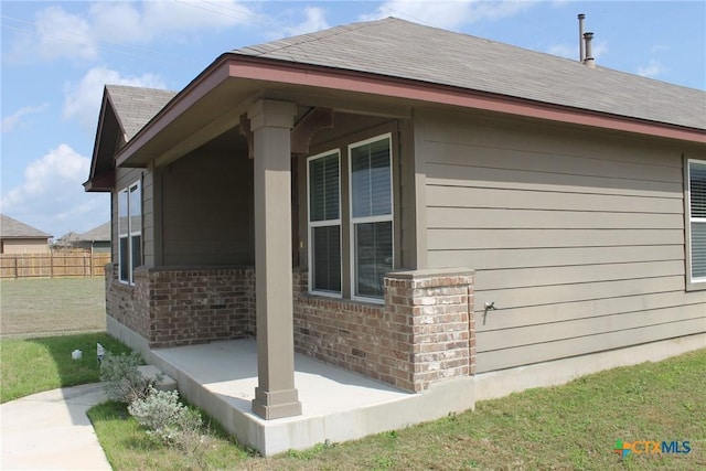 view of home's exterior featuring a yard, brick siding, a shingled roof, and fence