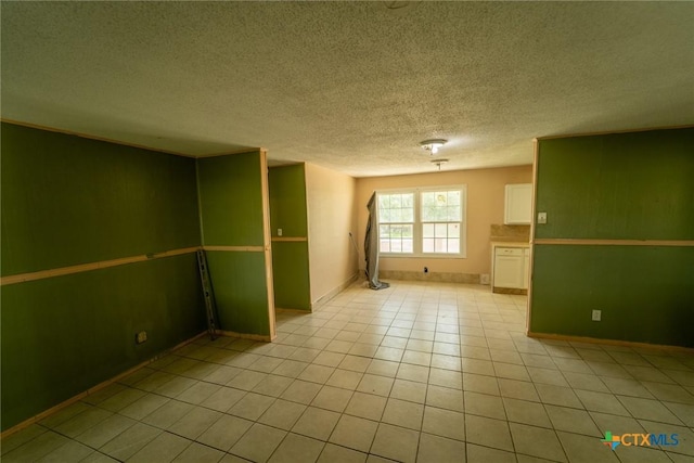 basement featuring light tile patterned flooring, a textured ceiling, and baseboards