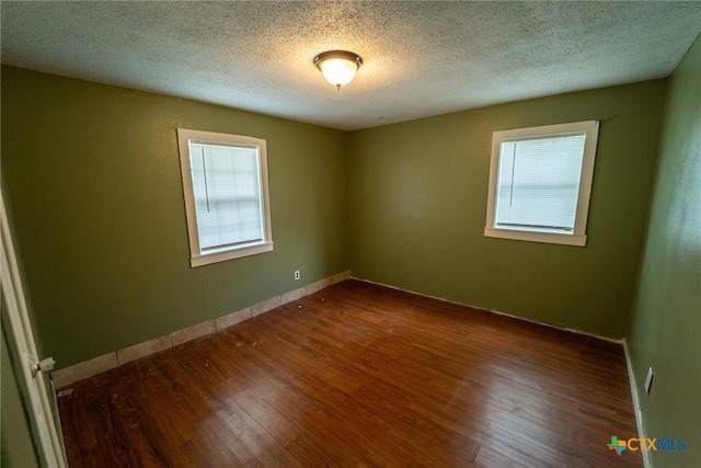 empty room with wood finished floors, a textured ceiling, and baseboards