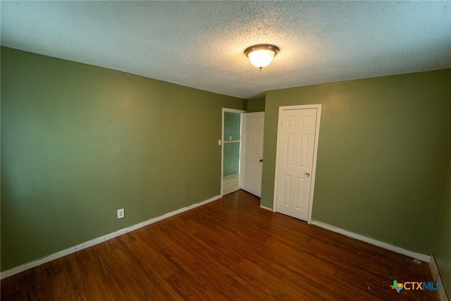 spare room with wood finished floors, a textured ceiling, and baseboards