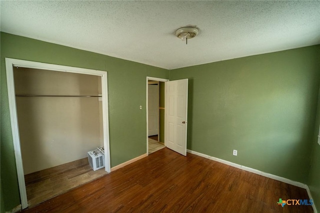unfurnished bedroom with a textured ceiling, wood finished floors, a closet, and baseboards