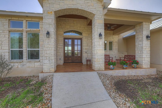 view of exterior entry featuring french doors, stone siding, covered porch, and a ceiling fan