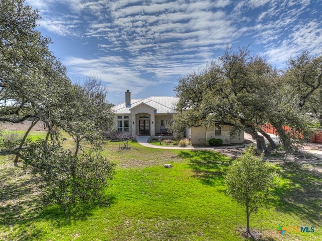 view of front facade with metal roof, stone siding, french doors, a front lawn, and a chimney