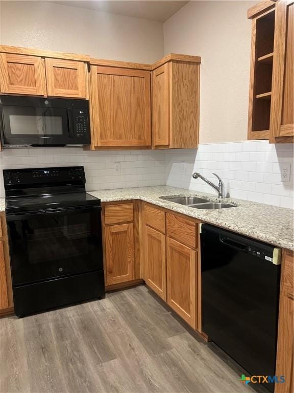 kitchen with black appliances, sink, decorative backsplash, light stone counters, and wood-type flooring