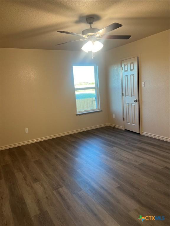 empty room with a textured ceiling, ceiling fan, and dark hardwood / wood-style floors