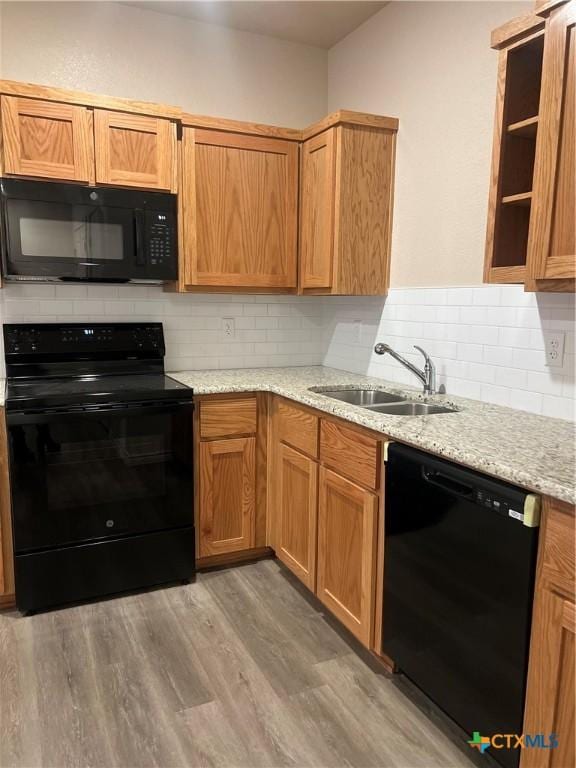 kitchen with light stone countertops, sink, wood-type flooring, decorative backsplash, and black appliances