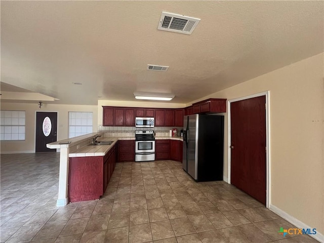 kitchen with sink, appliances with stainless steel finishes, tile patterned flooring, tasteful backsplash, and kitchen peninsula