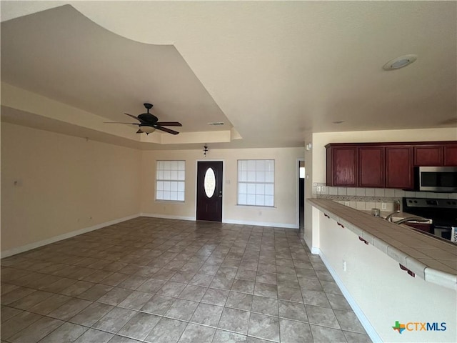 kitchen with range with electric stovetop, tile counters, a raised ceiling, ceiling fan, and backsplash