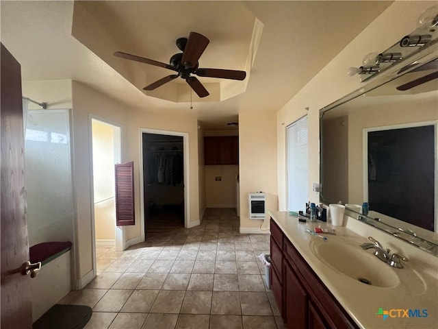 bathroom featuring ceiling fan, heating unit, vanity, a tray ceiling, and a shower