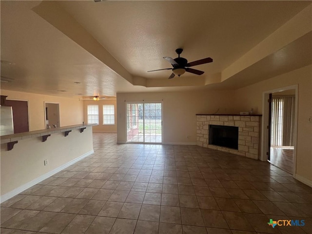 unfurnished living room with tile patterned floors, a fireplace, ceiling fan, and a tray ceiling