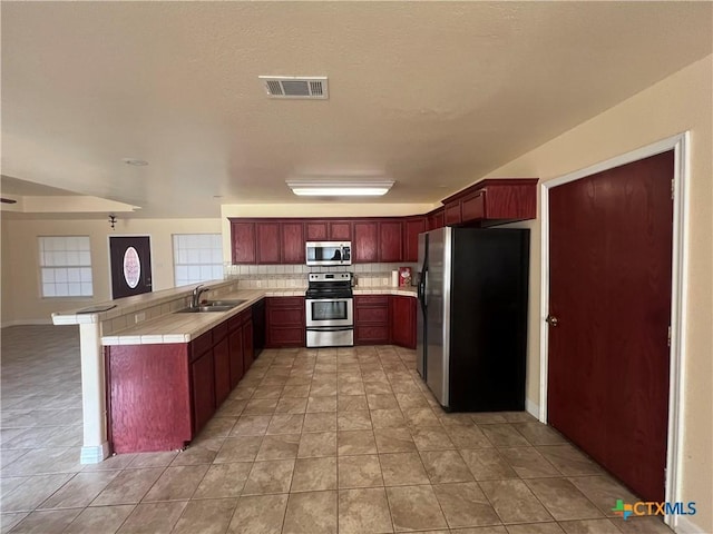 kitchen with sink, light tile patterned floors, kitchen peninsula, stainless steel appliances, and backsplash