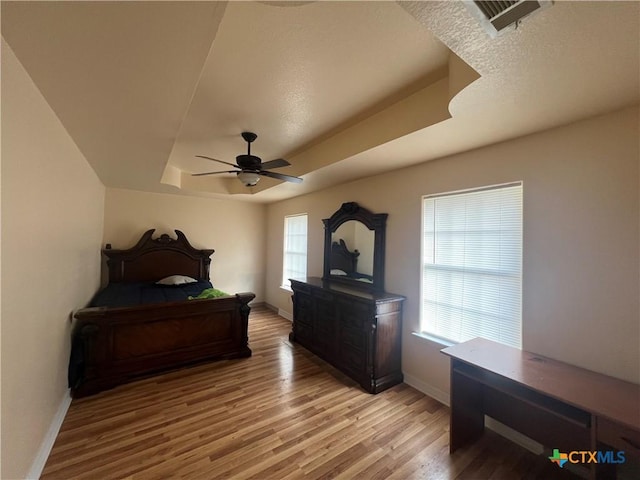 bedroom with a raised ceiling, ceiling fan, and light hardwood / wood-style flooring