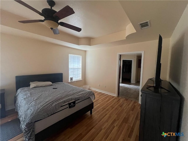 bedroom featuring a raised ceiling, dark wood-type flooring, and ceiling fan