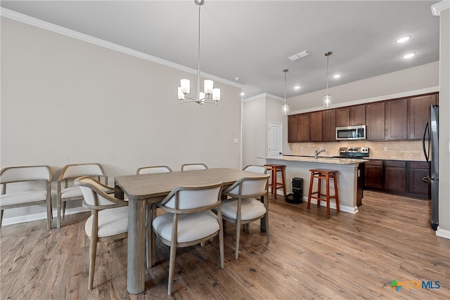 dining space with sink, light hardwood / wood-style flooring, a notable chandelier, and crown molding