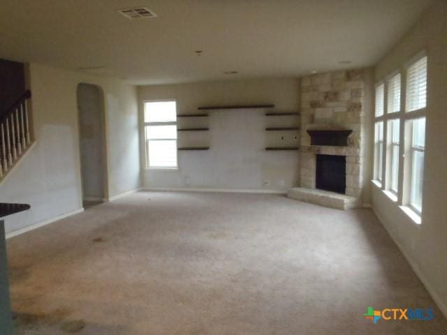 unfurnished living room featuring light colored carpet and a stone fireplace