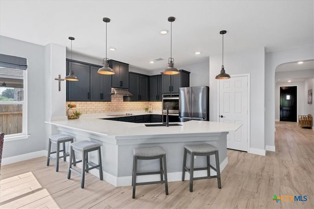 kitchen with appliances with stainless steel finishes, under cabinet range hood, a breakfast bar, a peninsula, and recessed lighting