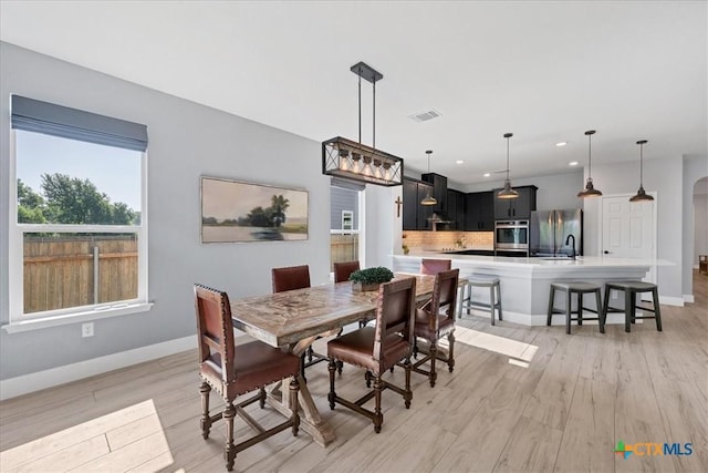 dining room with light wood finished floors, baseboards, recessed lighting, and arched walkways