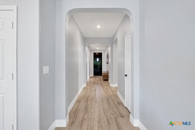 hallway featuring arched walkways, light wood-type flooring, and baseboards