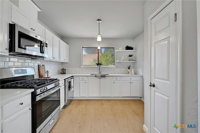 kitchen featuring white cabinetry, hanging light fixtures, stainless steel appliances, and light wood-type flooring