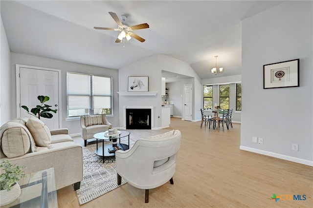 living room with ceiling fan with notable chandelier, light hardwood / wood-style floors, and lofted ceiling