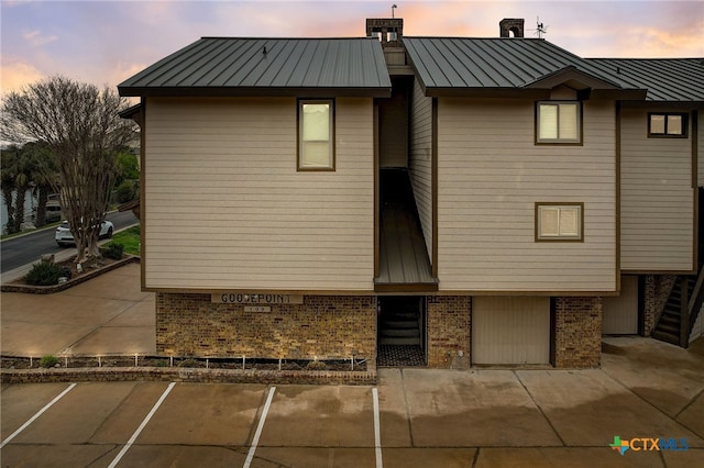 property exterior at dusk featuring uncovered parking, a standing seam roof, brick siding, and metal roof